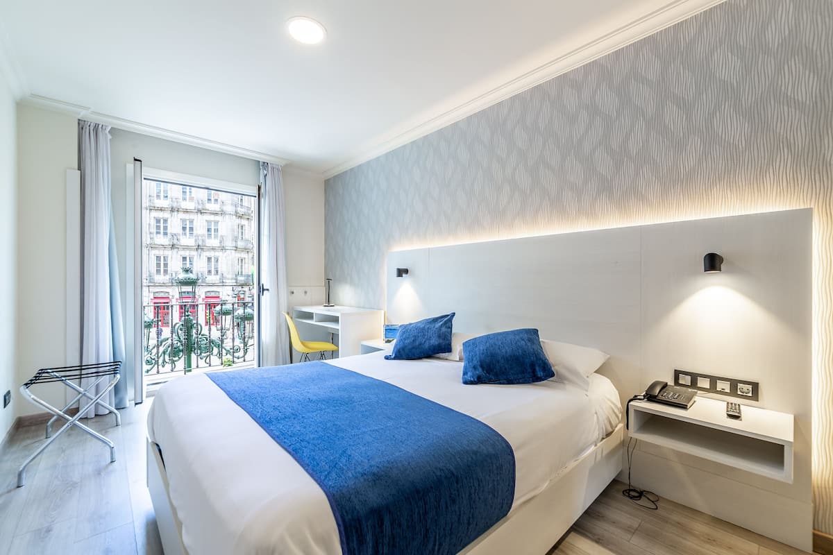 Ein modernes Hotelzimmer mit einem großen Bett, einem Schreibtisch und Blick auf eine Stadtlandschaft durch das Fenster.
