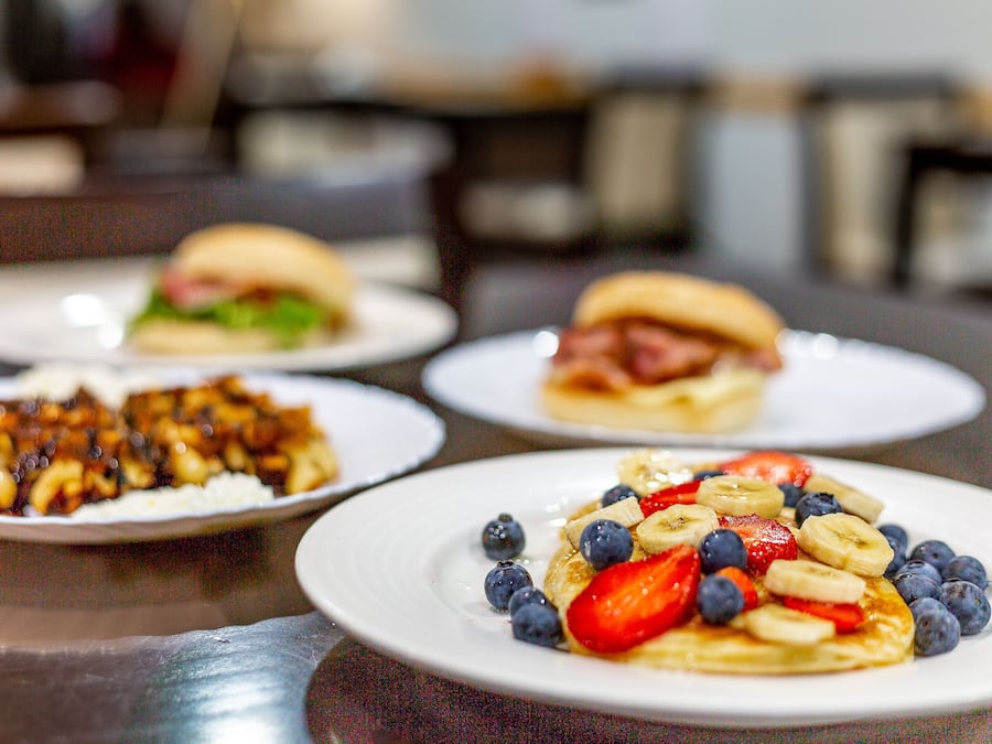 A dining table with plates of food, including pancakes with fruit and a burger.