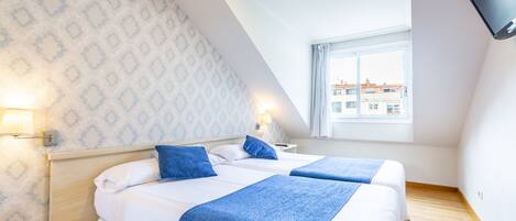 A hotel room with two beds, a TV mounted on the wall, and a window with a view of buildings.