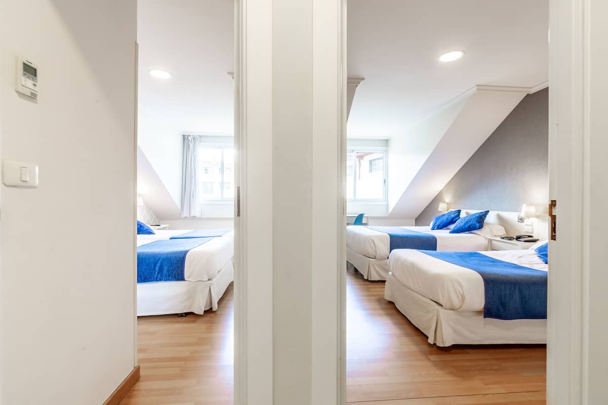 Ein Hotelzimmer mit zwei Betten, weißen Wänden, Holzboden und einer schrägen Decke mit Dachfenster.