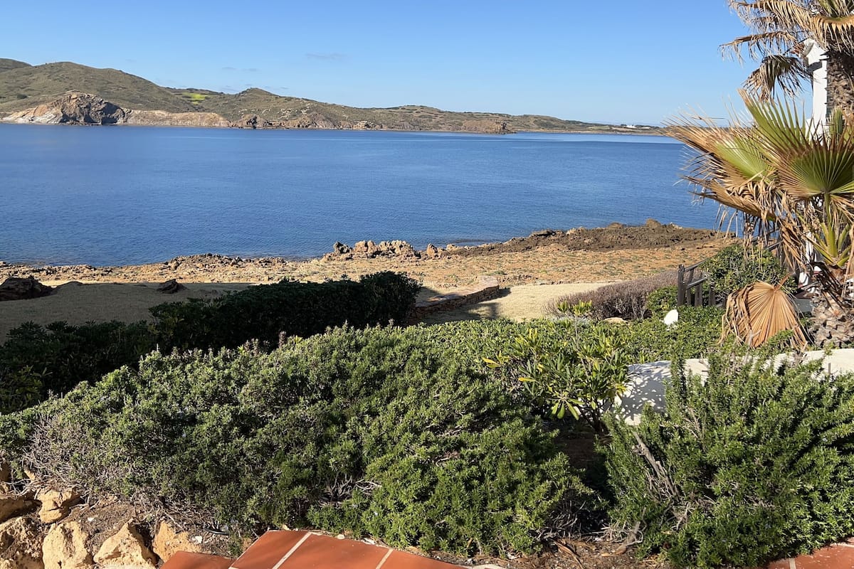 Ett kustlandskap med en klarblå himmel, en sandstrand, klippiga utskjutande partier och tät, grön vegetation.