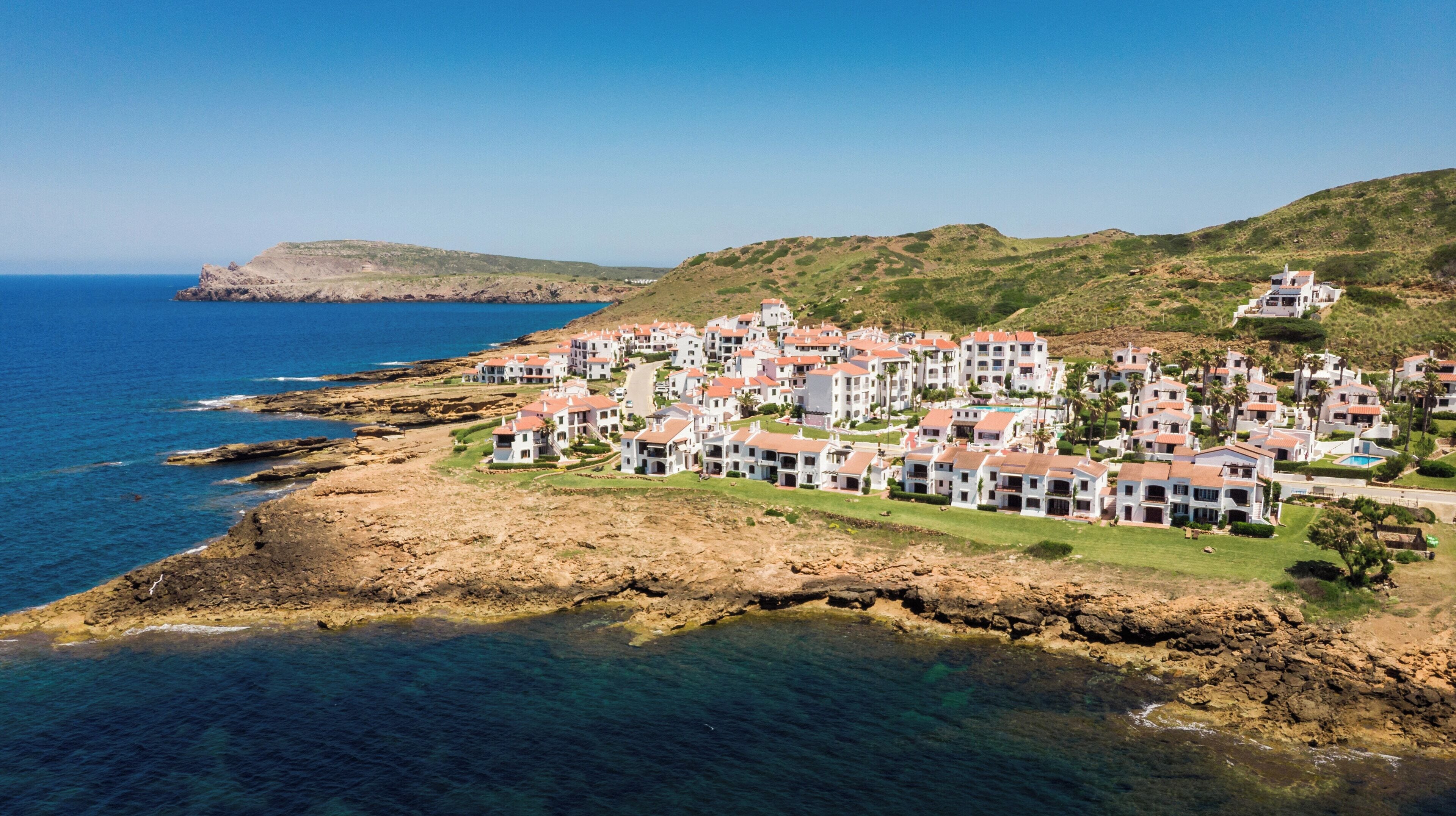 A coastal resort with white buildings, a rocky shoreline, and clear blue sea.