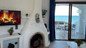 Een woonkamer met een open haard, een televisie en uitzicht op zee.