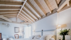 A bedroom with a wooden ceiling, two beds, a nightstand with a lamp, a chair, and a wall-mounted light fixture. - Hotel Palacio de Los Navas (Granada)