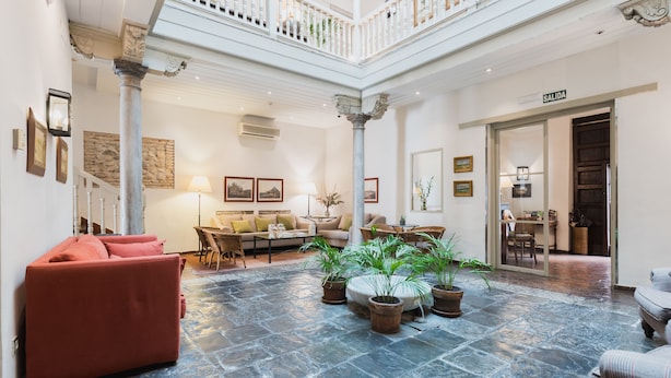 A spacious lobby with a high ceiling, stone flooring, and a central seating area with a sofa and chairs. - Hotel Palacio de Los Navas (Granada)