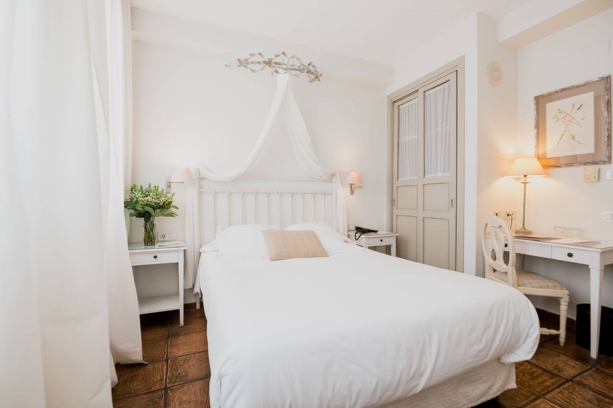 Un dormitorio con cama, mesitas de noche, escritorio, silla y lámpara.