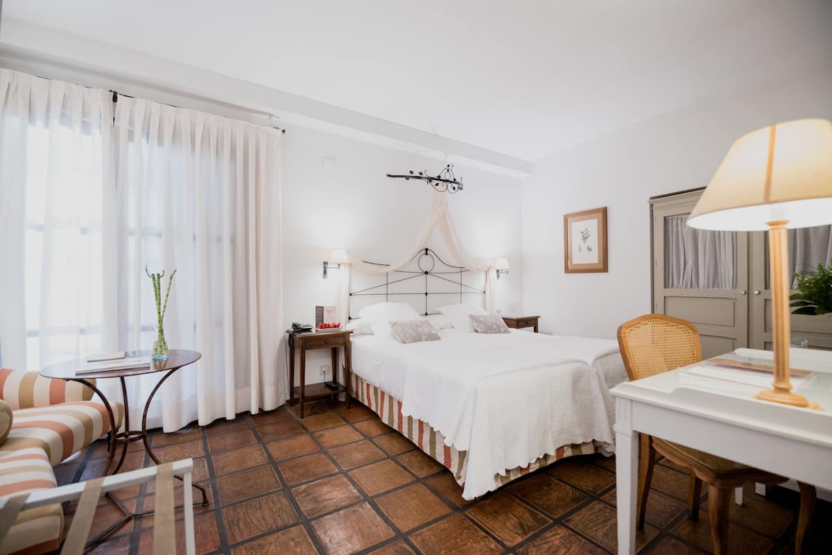 Una habitación de hotel con cama, mesitas de noche, una silla, escritorio y lámpara.