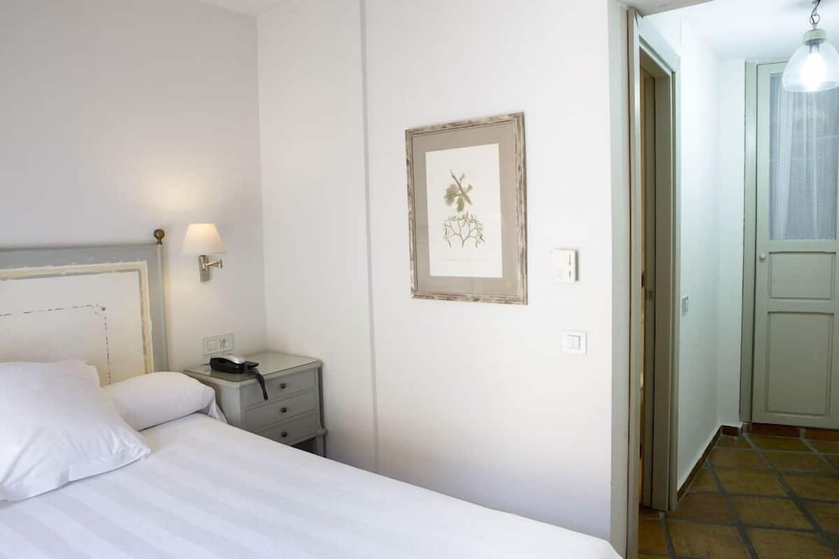 Un dormitorio con cama, mesita de noche, lámpara y una obra de arte botánica enmarcada en la pared.