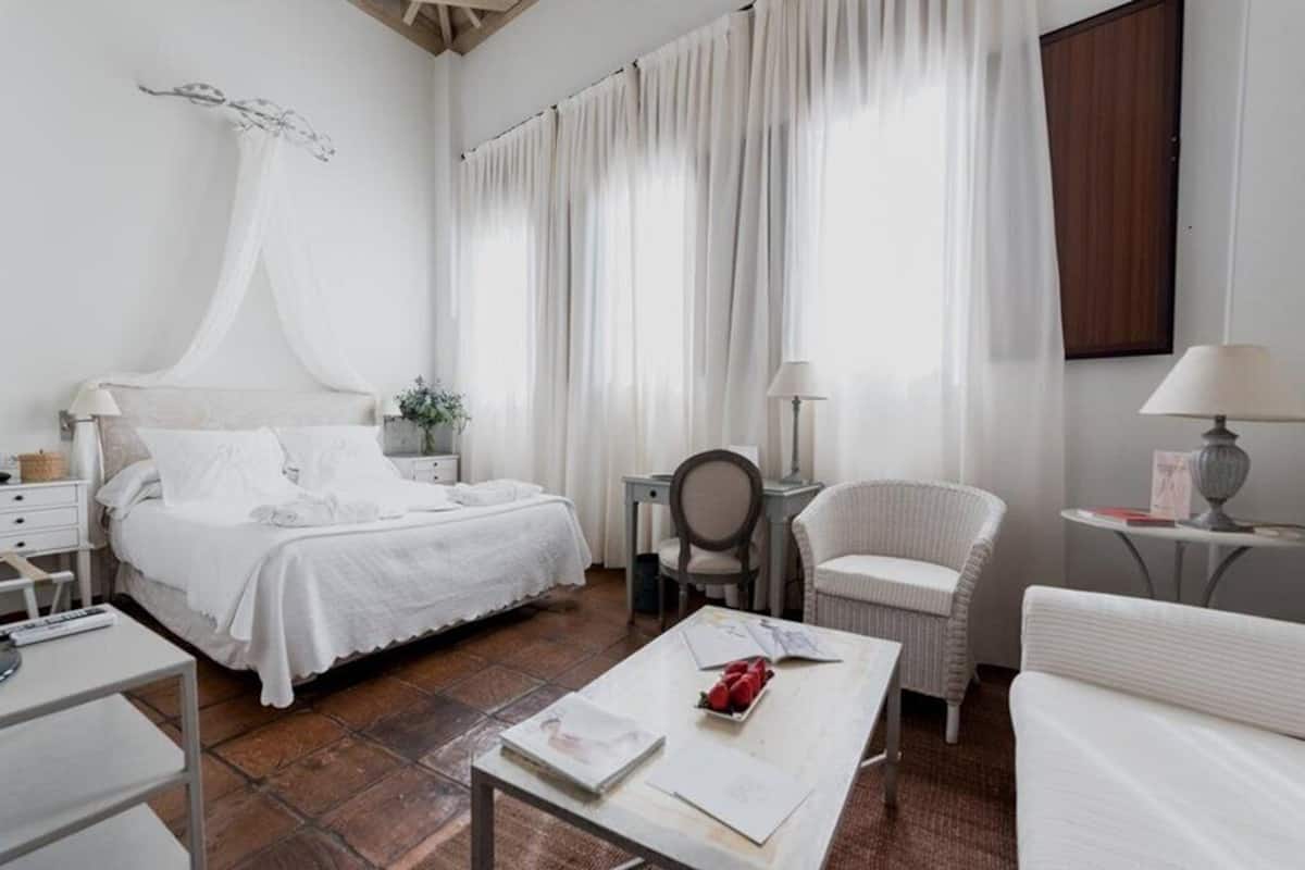 Un dormitorio con cama, mesita de noche, silla y una pequeña mesa con un libro y un florero.