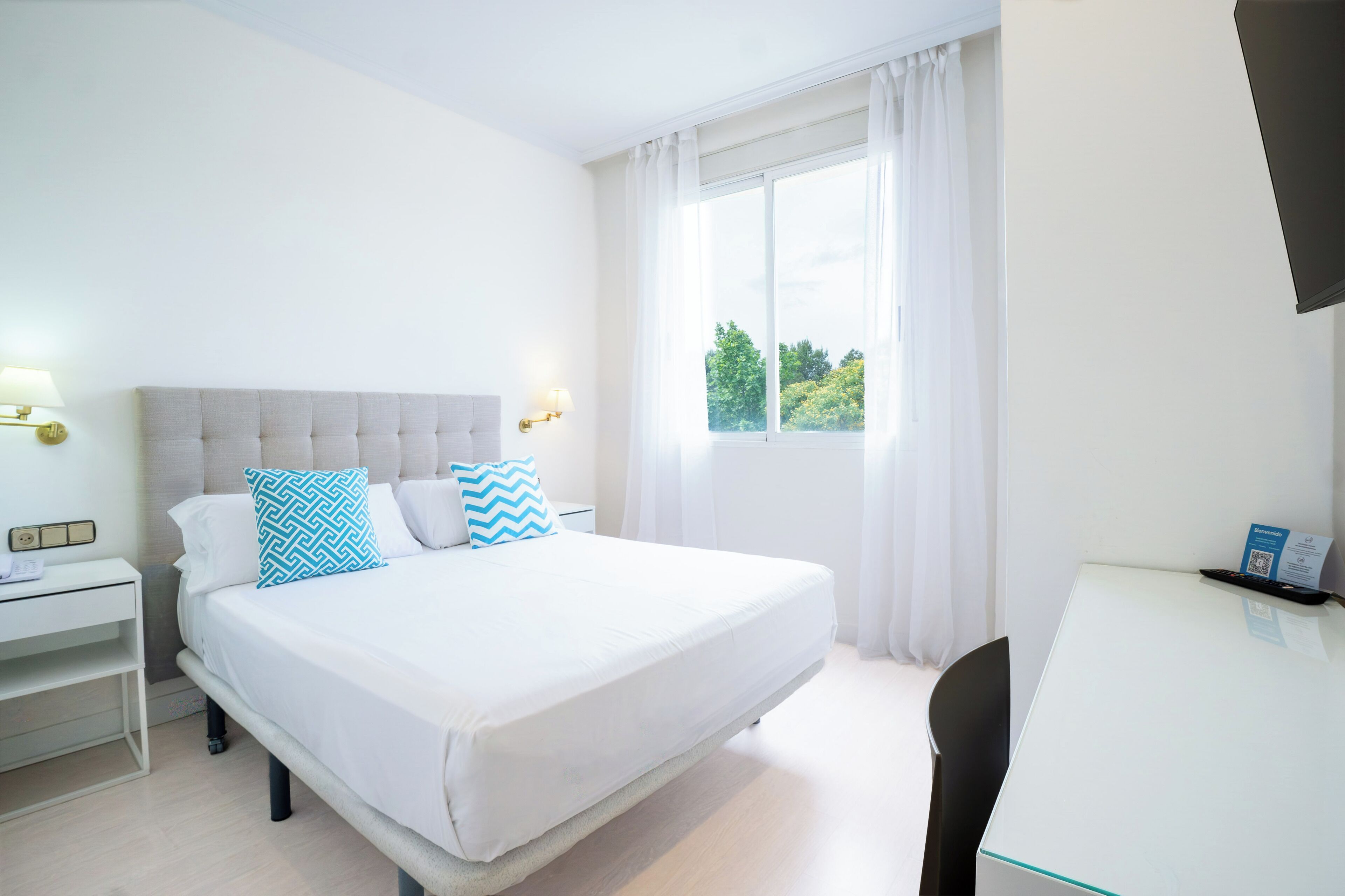 Habitación de hotel con cama, escritorio, silla, mesita de noche y ventana con cortinas.