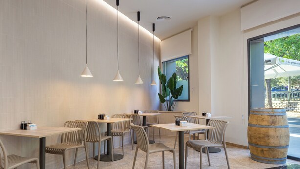 Et moderne restaurantinteriør med høje borde, stole, hængende lamper og et stort vindue med udsigt ud