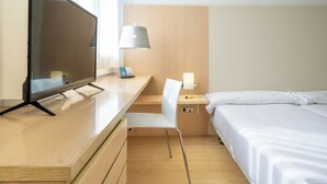 Et hotelværelse med et træskrivebord, en stol, en seng og et natbord med en lampe.