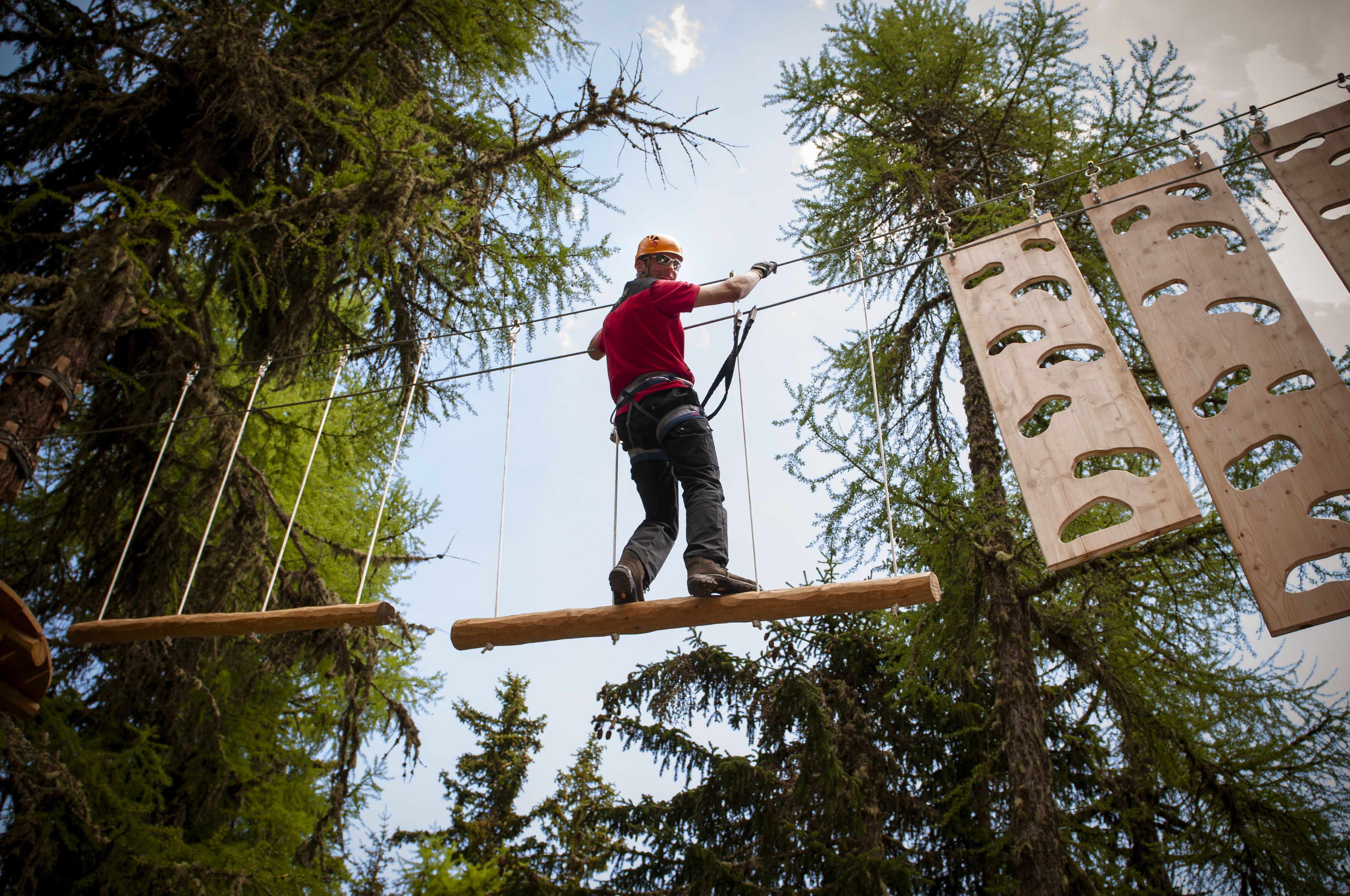 A person on a suspended platform in a forested area, wearing safety gear.