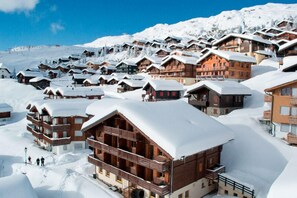 Un resort cubierto de nieve con varias edificaciones de madera, balcones y un telón de fondo montañoso.