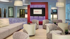 A modern hotel lobby with a reception desk, seating area with patterned sofas and armchairs, and a large screen displaying the hotel name. -  IntercityHotel Frankfurt Airport Terminal 3 (Frankfurt)