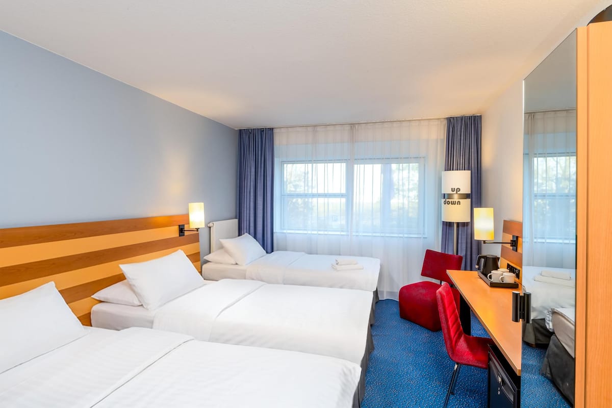 Quarto de hotel com duas camas, uma mesa, uma cadeira e um espelho grande.