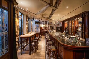 A bar area with stools, a counter with bottles, framed pictures on the walls, and a patterned floor.
