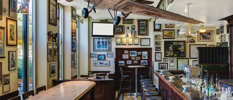 Un bar avec des tables et des chaises en bois, un comptoir où sont exposées des bouteilles, et un plafond orné d’une grande maquette d’avion.