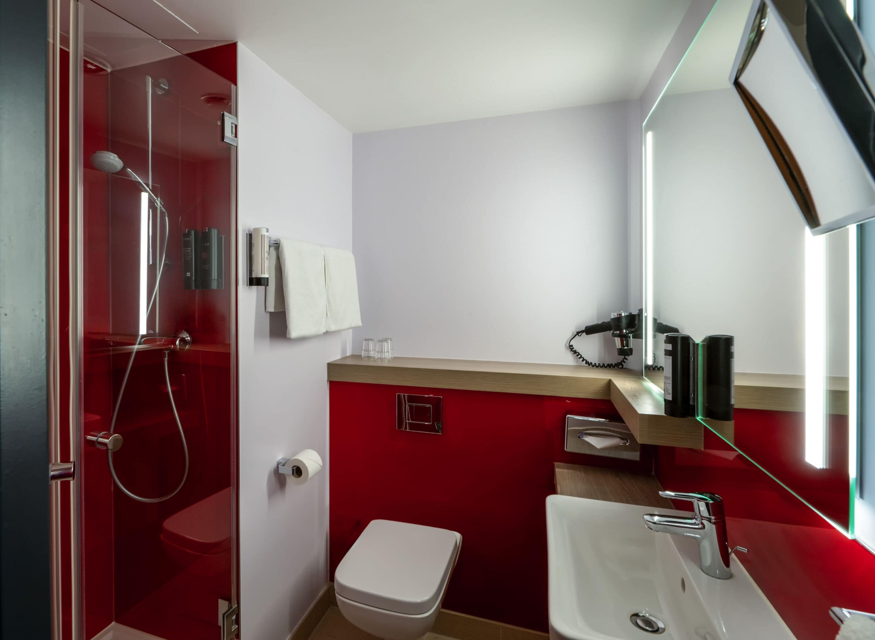 A modern bathroom with a glass-enclosed shower, a white toilet, a sink with a mirror, and red walls.