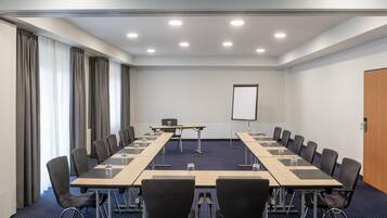 Ein Konferenzraum mit langem Tisch, Stühlen, einer Projektionsleinwand und einer Whiteboard-Tafel.