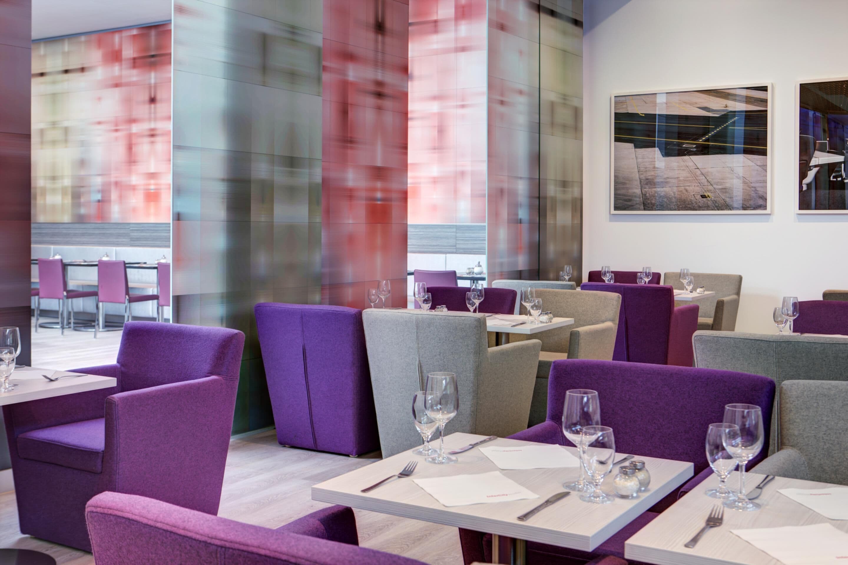 Un restaurante moderno con asientos morados y grises, mesas blancas y divisiones de vidrio transparente.