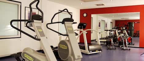 A gym with cardio machines, mirrors, and a red accent wall.