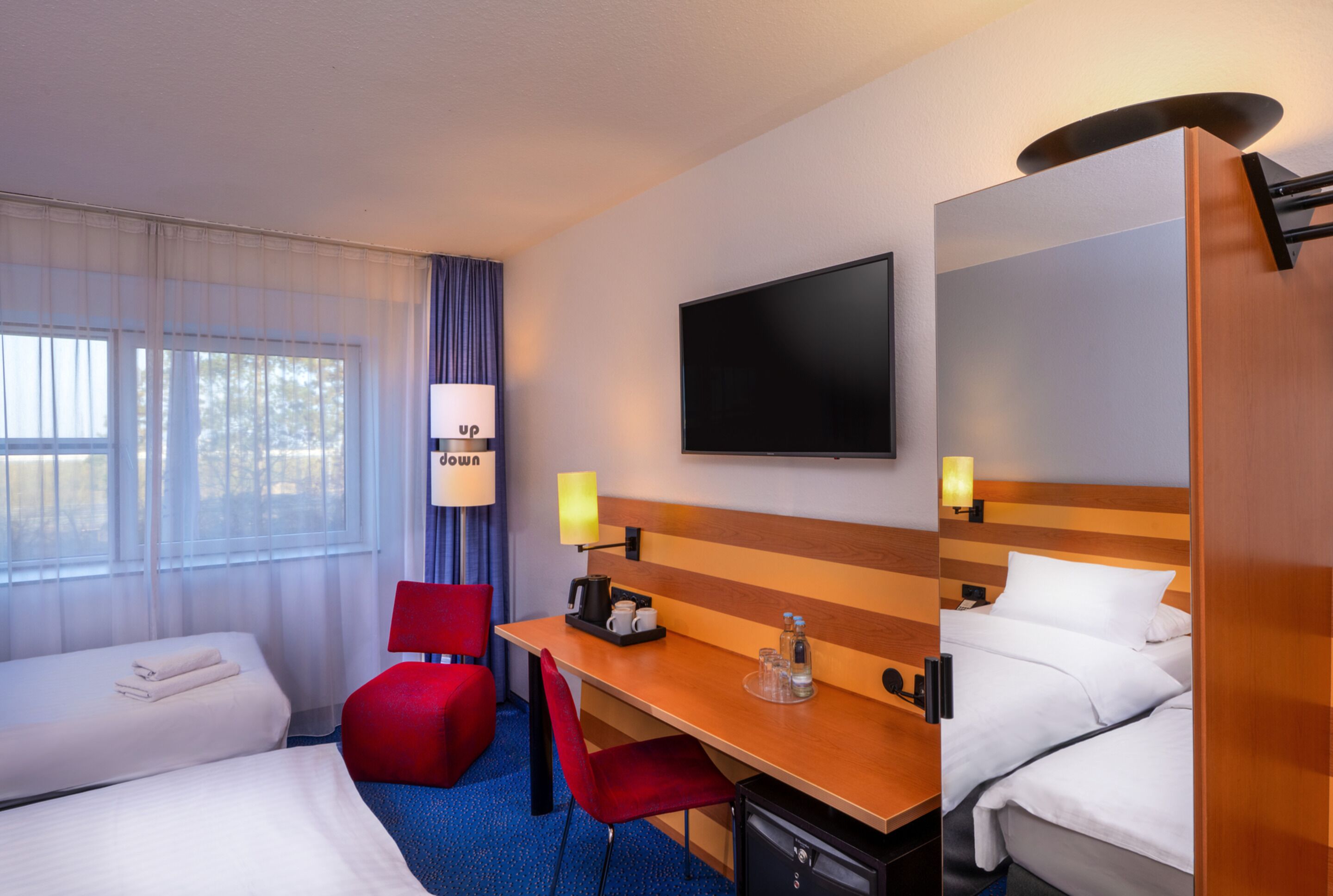 A hotel room with two beds, a desk, a chair, a TV, and a window with curtains.