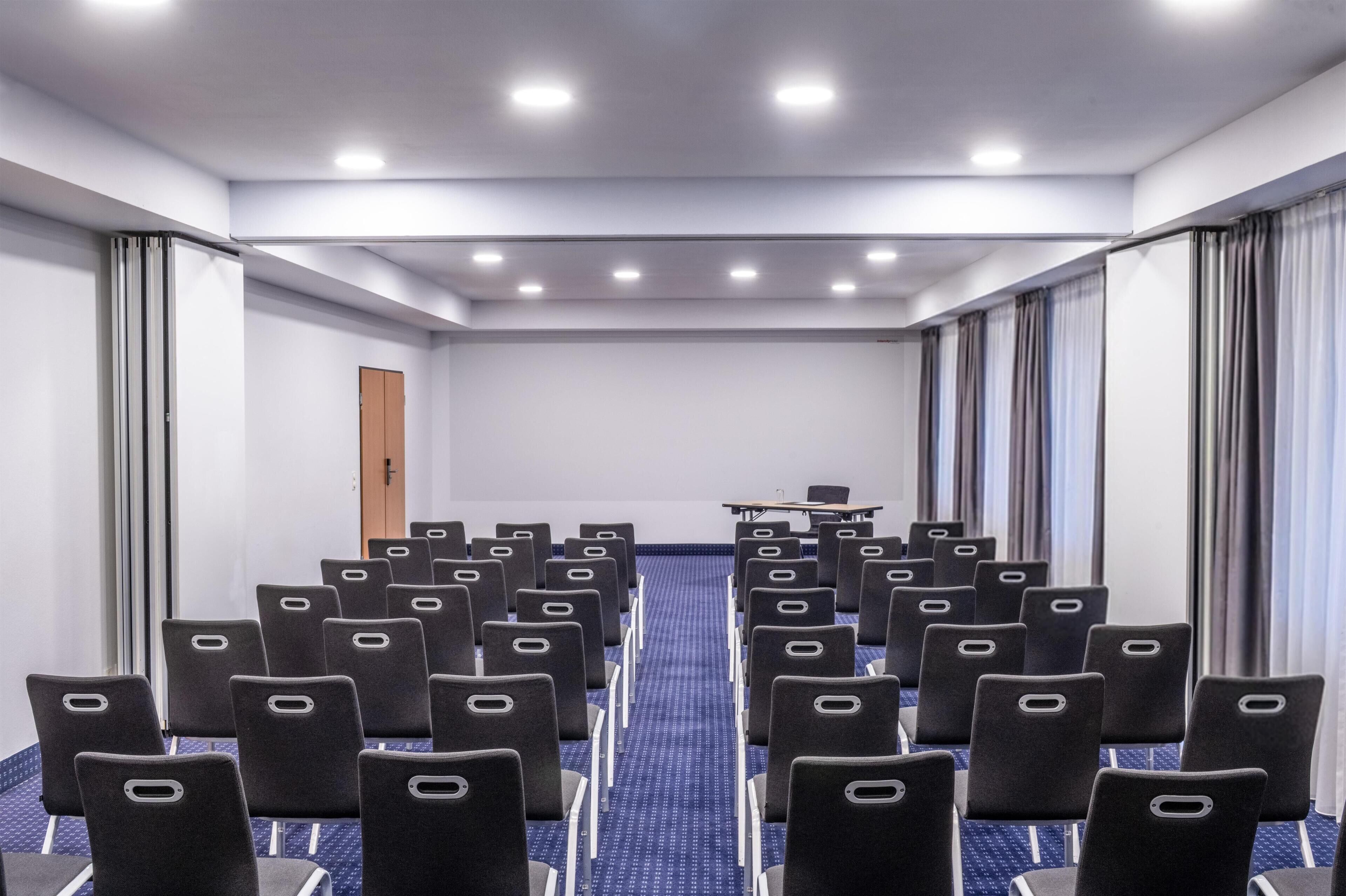 Un salón de conferencias con filas de sillas, una mesa y una puerta.