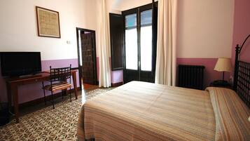 A hotel room with a bed, a desk with a chair, a television, and a window with curtains.