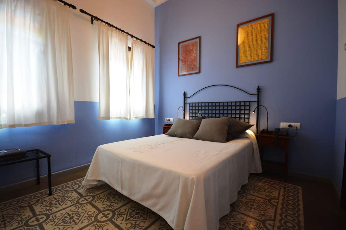 A bedroom with a bed, curtains, a nightstand, and a wall with two framed pictures.