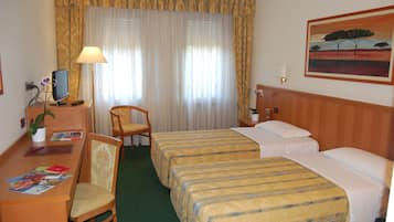 A hotel room with two single beds, a desk with a chair, a TV, and a painting on the wall.