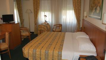 Een hotelkamer met een bed, een bureau, een stoel, een lamp en een schilderij aan de muur.