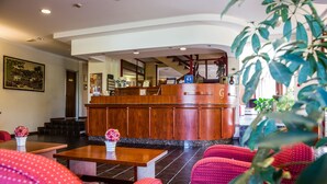 A reception area with a wooden counter, a staircase, and red upholstered chairs. - Hotel Galant (Venaria Reale)