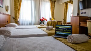 A hotel room with two beds, a laptop on one bed, a table with a vase of flowers, and a television on the wall. - Hotel Galant (Venaria Reale)