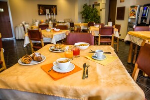 Uma sala de jantar com mesas preparadas para o café da manhã, incluindo croissants, café e suco de laranja.