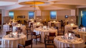 A restaurant with round tables set for dining, featuring candle centerpieces and a modern ceiling design. - Enea Hotel Aprilia (Aprilia)