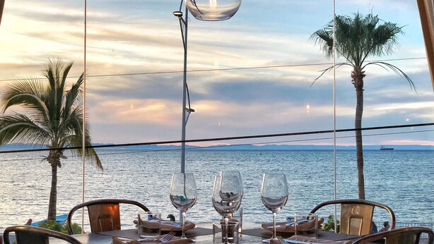 A dining table set for two with a clear view of the sea and a sunset in the background. - Posada De Las Flores La Paz (La Paz)