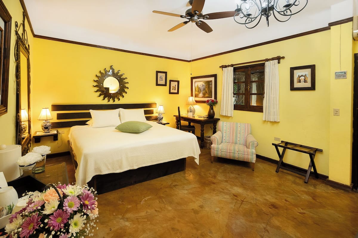 Una habitación de hotel con una cama, una silla, una mesa y un ventilador de techo.