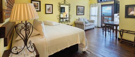 A bedroom with a bed, a nightstand, a lamp, a mirror, and a window with a view.