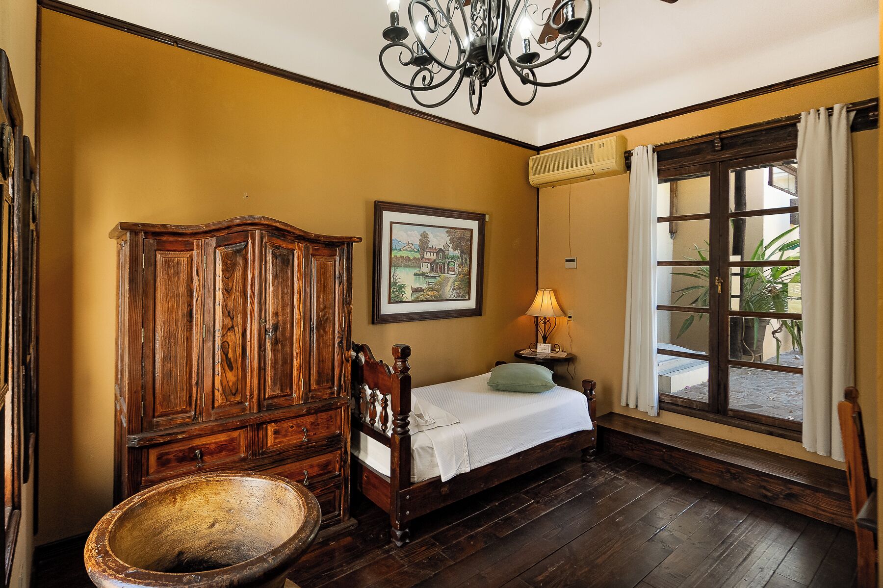 Una habitación con una cama de madera, un armario de madera, un cuadro en la pared y una ventana con vistas a la vegetación.