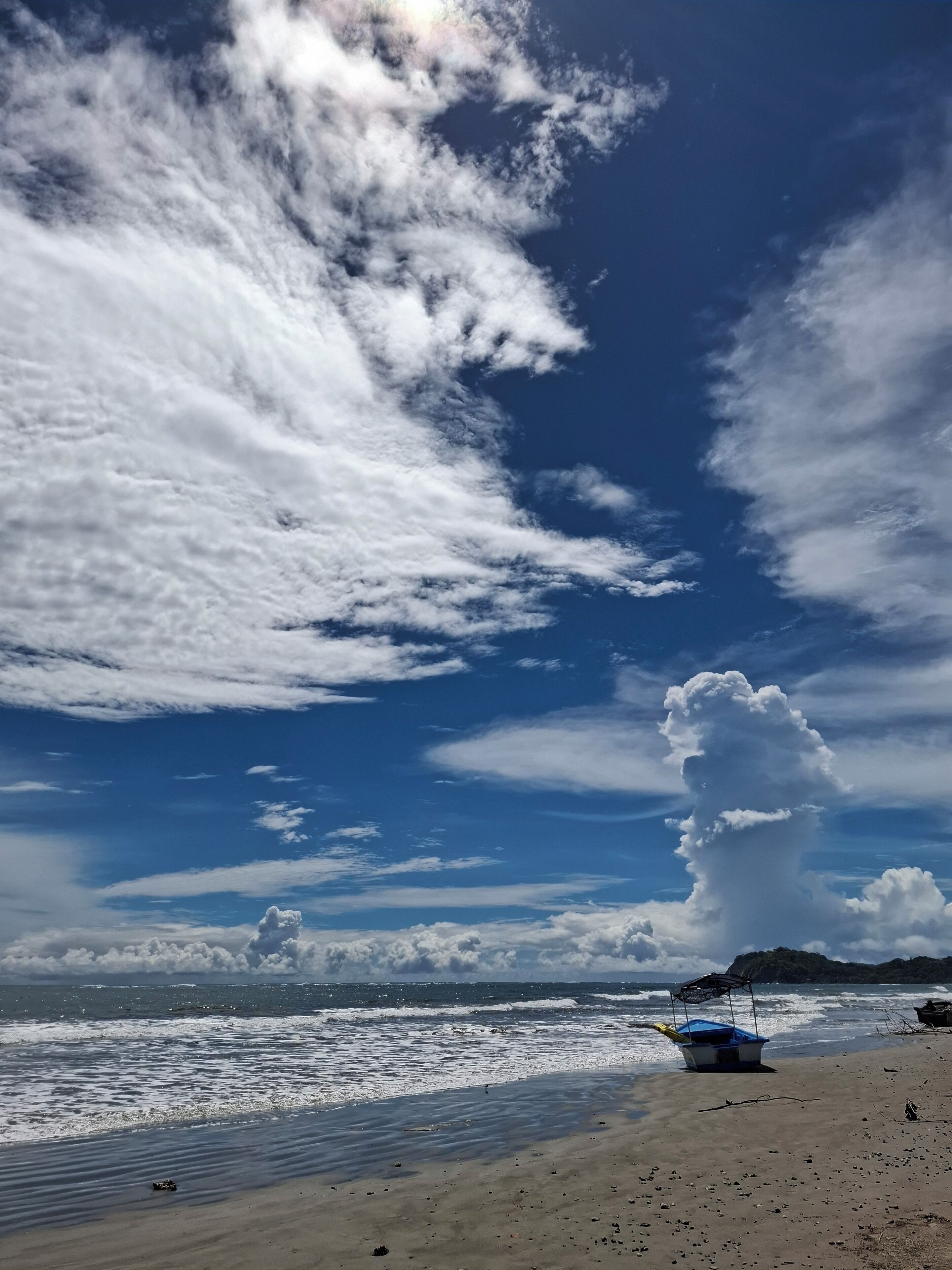 A beach with a boat on the sand and a clear sky with clouds.