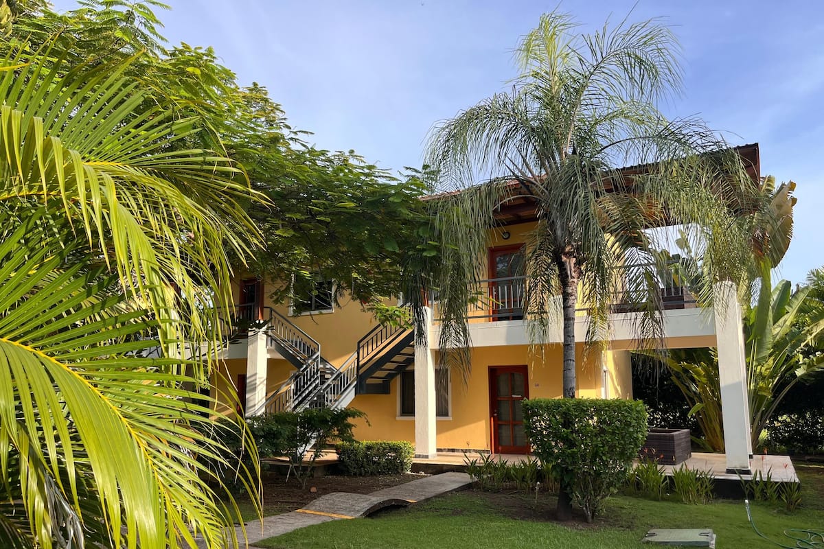 A two-story building with a yellow facade, a balcony, and a staircase leading to the upper floor.