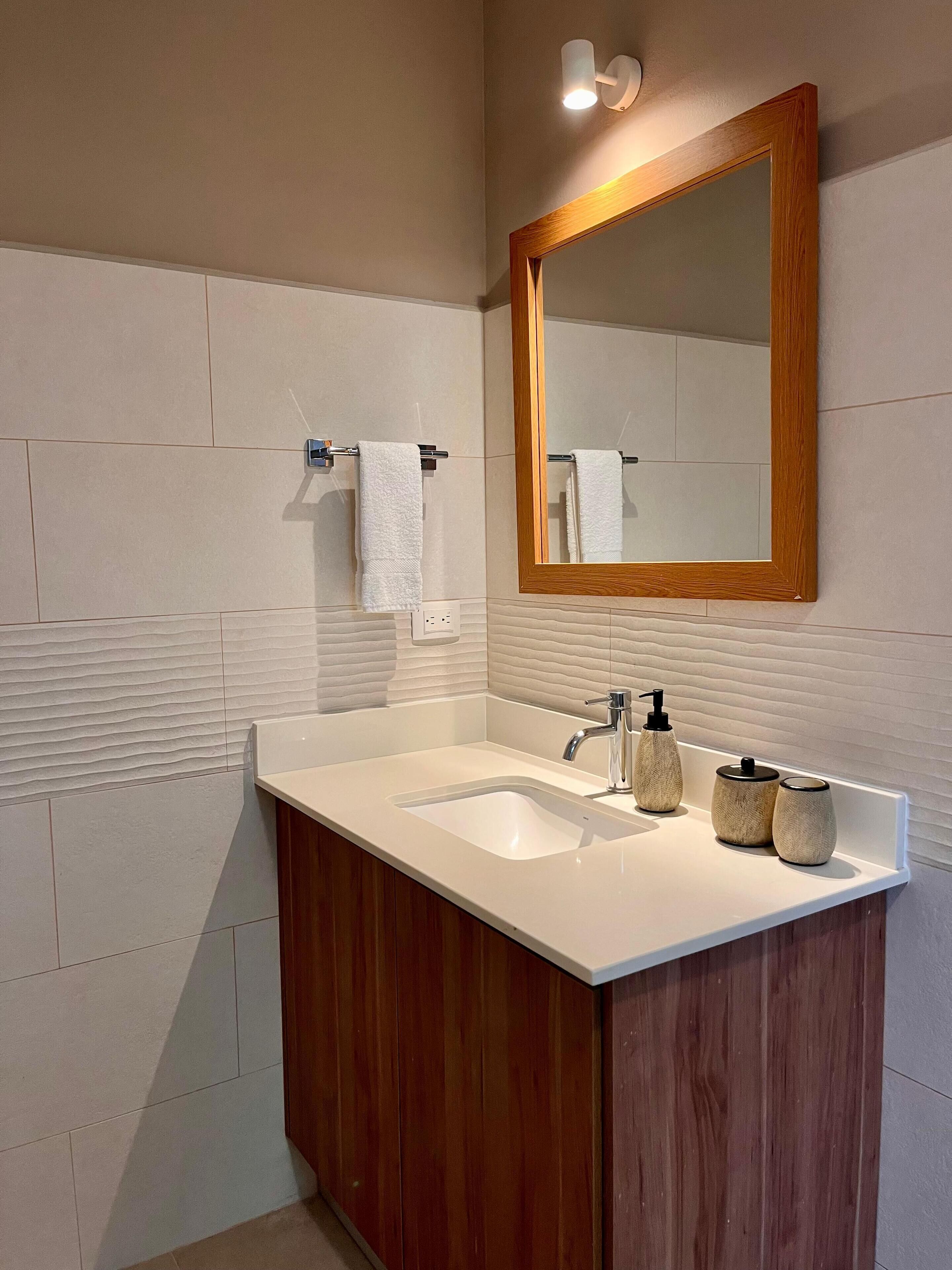 A modern bathroom with two sinks, wooden cabinets, a large mirror, and a towel rack.