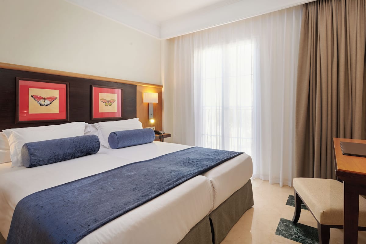 A hotel room with a large bed, two framed butterfly pictures, a desk, and a TV.
