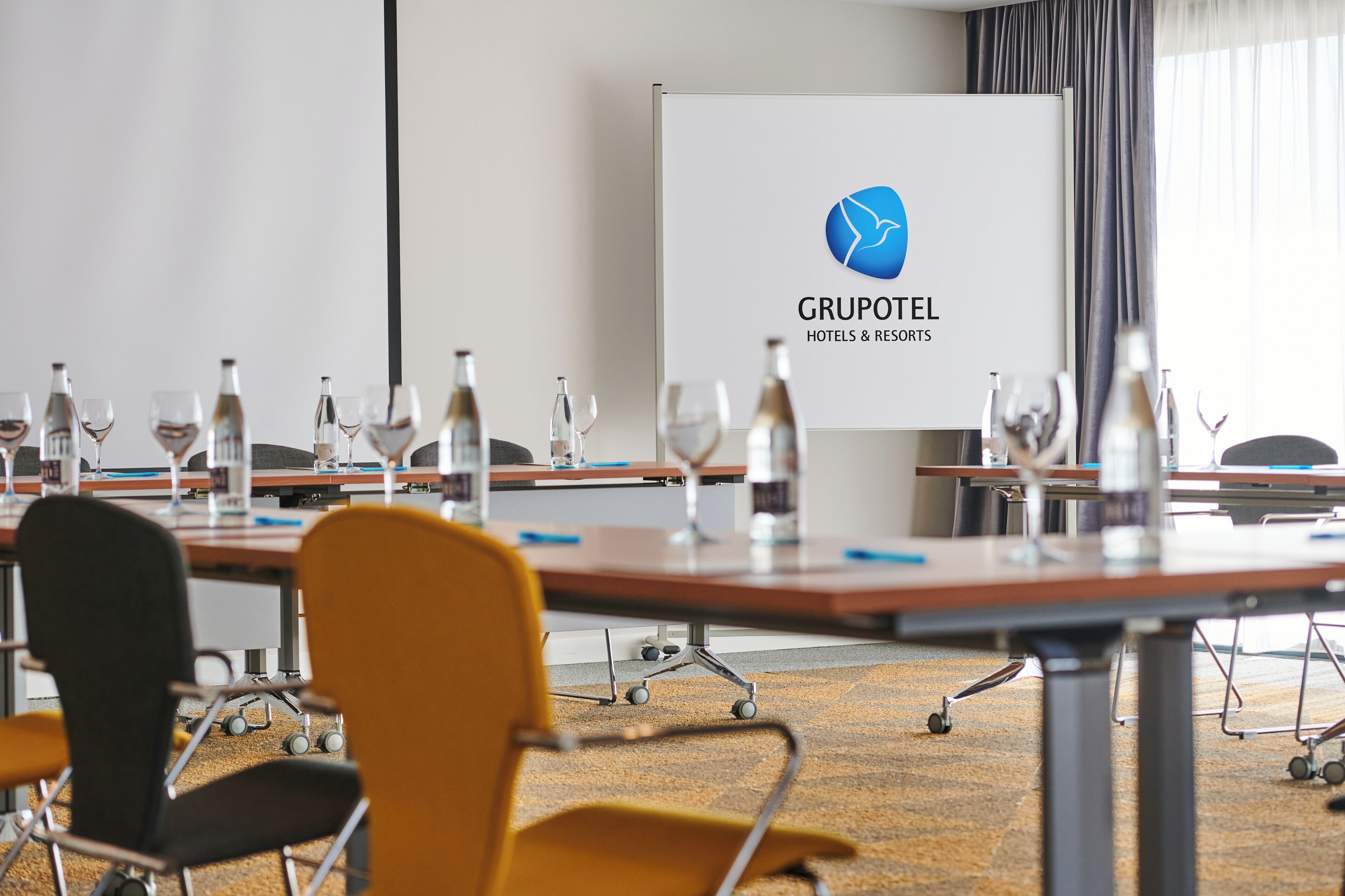 Un salón de conferencias con mesas, sillas y una pizarra mostrando el logotipo de Gruptotel.