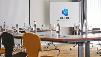 Un salón de conferencias con mesas, sillas y una pizarra mostrando el logotipo de Gruptotel.
