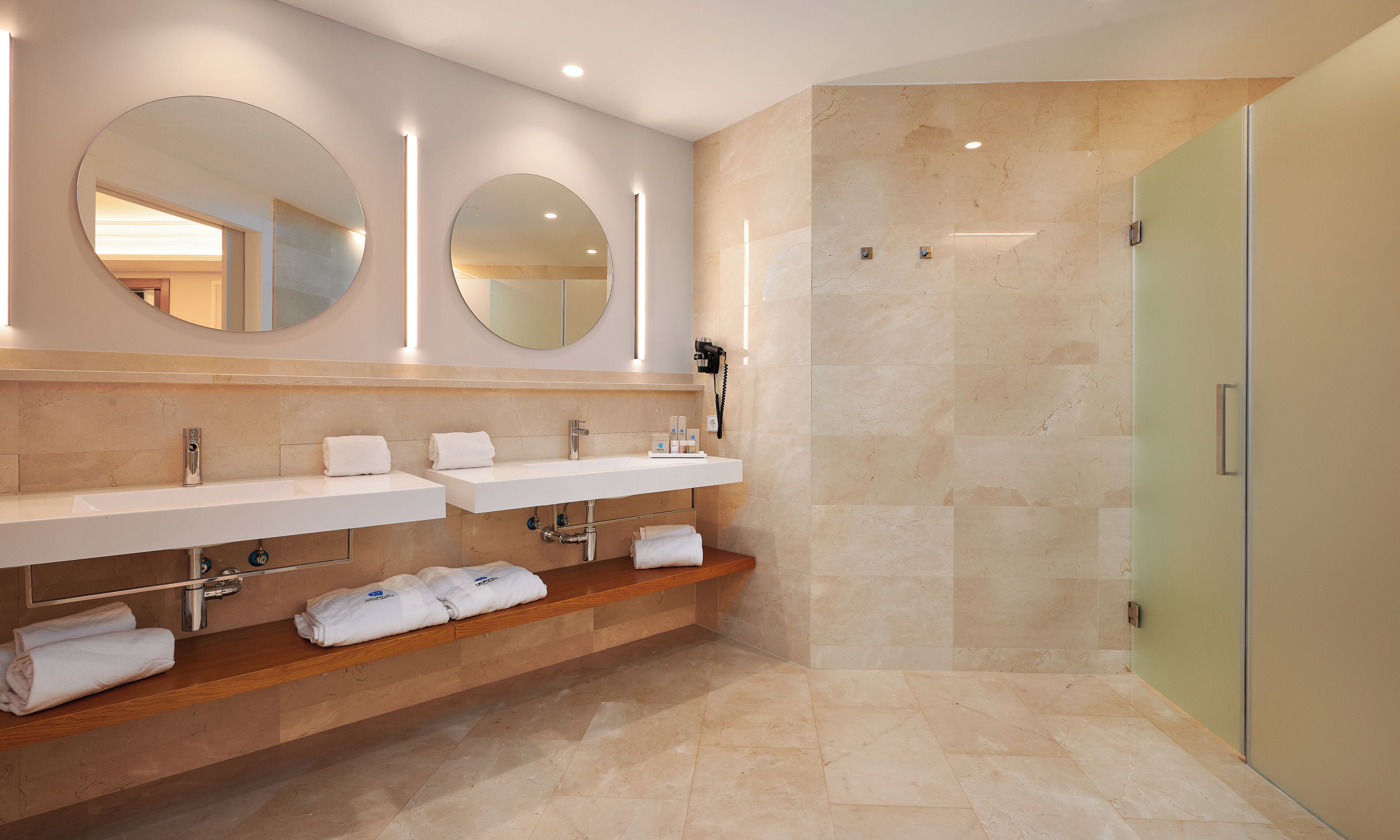 A modern bathroom with two sinks, a mirror, and a shower area.