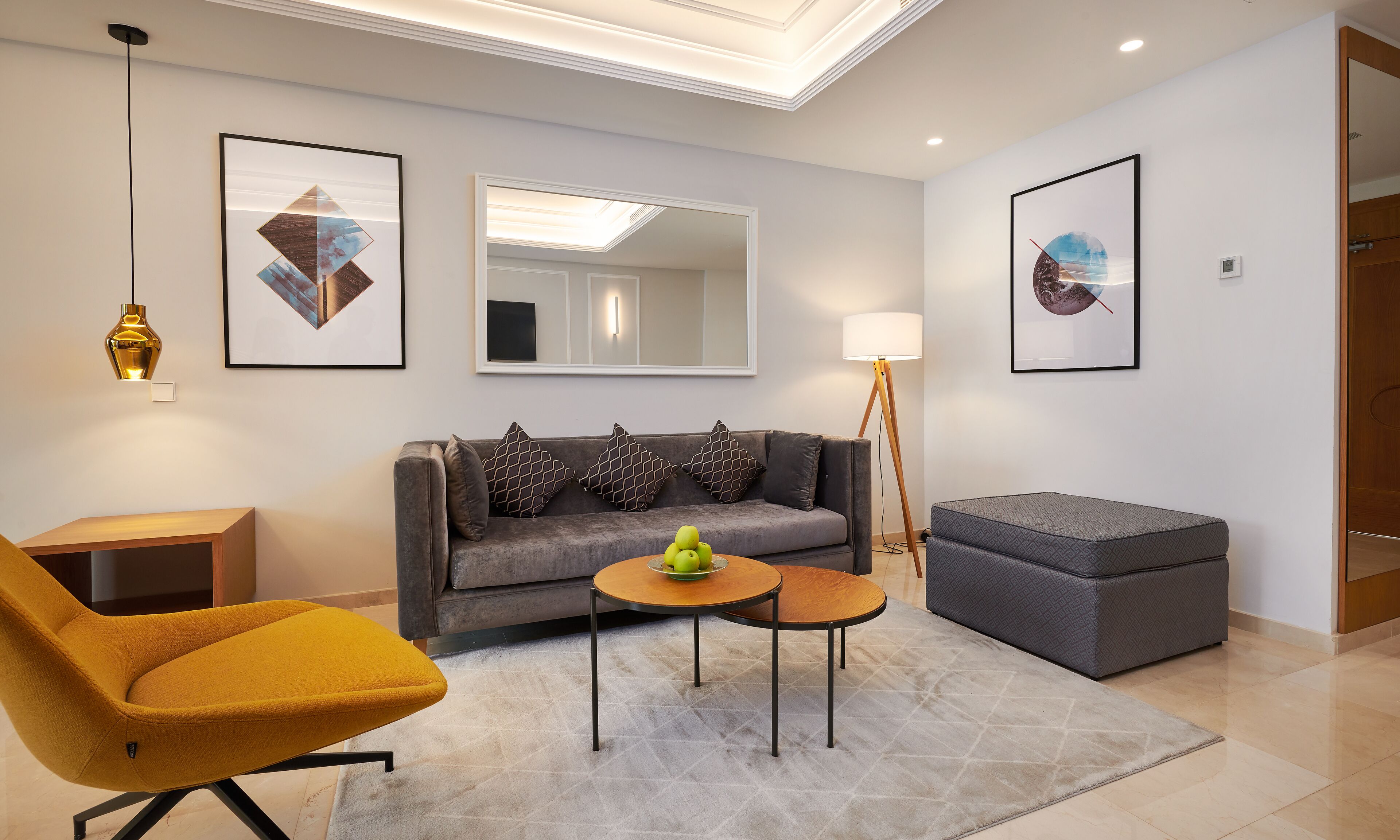 A modern living room with a sofa, a yellow armchair, a small round table with apples, and a floor lamp.