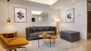 Una sala de estar moderna con un sofá, un sillón amarillo, una pequeña mesa redonda con manzanas y una lámpara de pie.