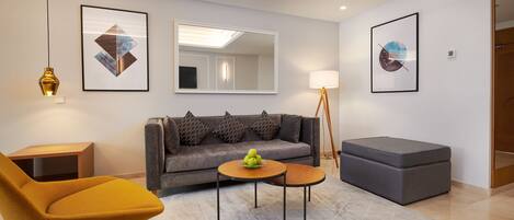 A modern living room with a sofa, a yellow armchair, a small round table with apples, and a floor lamp.